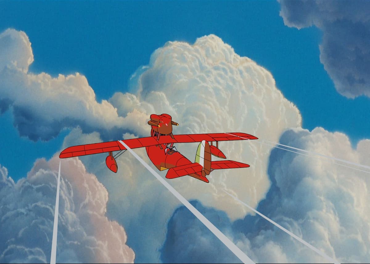 A red biplane flies through a cloudy blue sky, leaving white contrails.