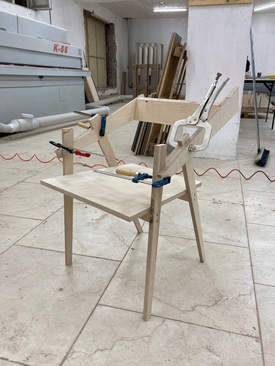 Wooden chair frame being assembled with clamps in a workshop.